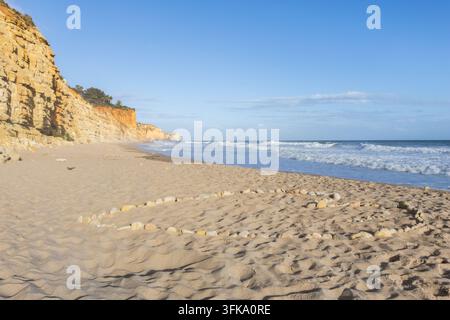 Eine große herzförmige Formation aus Steinen im Sand befindet sich an einem schönen Sandstrand in Lagos, Portugal, eingerahmt von dramatischen Küstenklippen und th Stockfoto