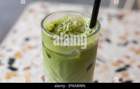 lebendiges Eismatcha-Latte mit schaumigen Bläschen und einem schwarzen Strohhalm, serviert auf einem modernen Terrazzo-Tisch in einer gemütlichen Café-Atmosphäre Stockfoto