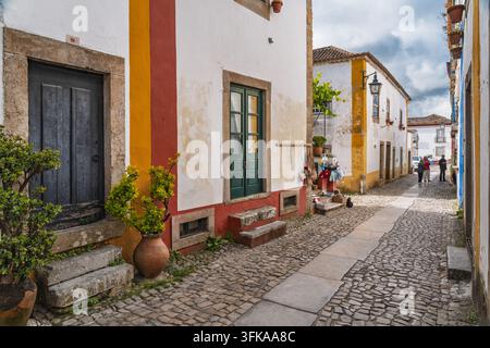 Obidos, Bezirk Leiria, Portugal - 13. Mai 2026: Blick auf historische Kopfsteinpflasterstraßen, die von traditionellen weißen Häusern gesäumt sind, die lebhafte rote und gelbe Farben aufweisen Stockfoto
