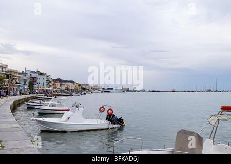 Zante Town, Griechenland, 1. September 2026: Uferpromenade des Hafens mit kleinen Booten, die entlang des Steinstegs festgemacht sind, und Yachten in der Marina, während Fußgänger vorbeigehen Stockfoto