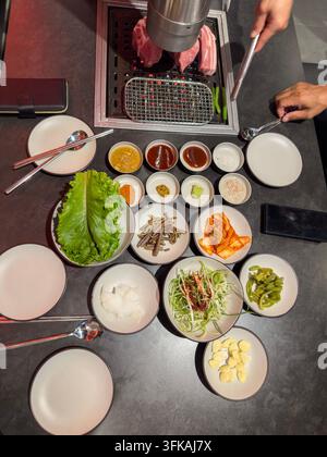 Koreanischer Barbecue-Tisch mit gegrilltem Schweinefleisch und traditionellen Beilagen Stockfoto