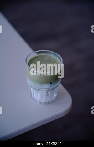 Eis-Matcha-Grüne-Tees-Latte serviert in einem klaren gerippten Glas auf dem Tisch im Café. Stockfoto