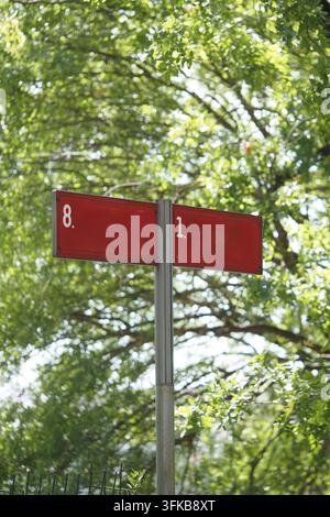 Rotes Straßenschild mit Zahlen unter hellgrünen Bäumen im Park Stockfoto