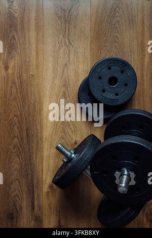 Schwarze verstellbare Hanteln und Hantelscheiben auf einem Holzfußbodenhintergrund mit Kopierplatz für Fitness-Trainingsdesign. Vertikales Format. Stockfoto