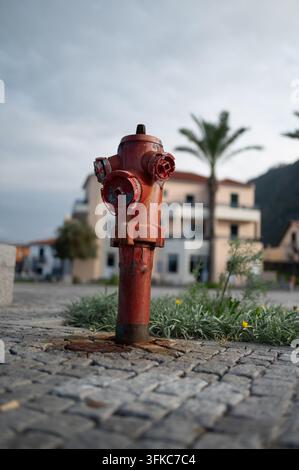 Eine Niedrigwinkel-, Nahaufnahme eines alten, verwitterten roten Feuerhydranten, der auf einem Kopfsteinpflaster steht. Der Hydrant zeigt abblätternde Farbe, Rost und Stockfoto