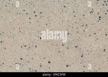 Nahaufnahme einer beigen Betonoberfläche mit feinen dunklen Gesteinsmehlpartikeln, die eine dezente gesprenkelte Textur erzeugen. Stockfoto