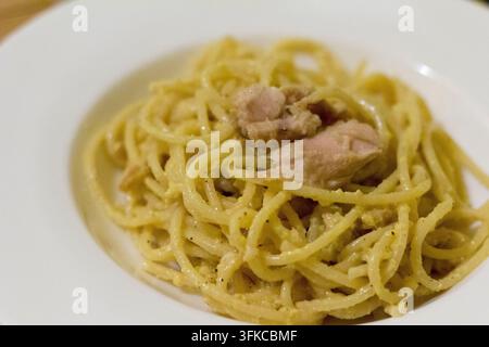 Spaghetti mit cremigem Kürbis-Pesto und Thunfischstücken auf einem weißen Teller, 45-Grad-Nahaufnahme, Bambusmatte am Rand, weiche Schärfentiefe Stockfoto