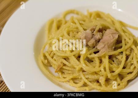 Spaghetti mit cremigem Kürbis-Pesto und Thunfischstücken auf einem weißen Teller, 45-Grad-Nahaufnahme, Bambusmatte am Rand, weiche Schärfentiefe Stockfoto