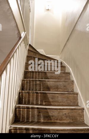Niedrigwinklige Ansicht einer schmalen antiken Holztreppe, die nach oben führt, mit weiß gestrichenen Wänden, Holzstufen und Holzgeländer in einem historischen Haus i Stockfoto