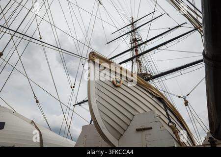 Niedrigwinkelaufnahme eines weißen hölzernen Rettungsboots, das auf dem Deckhaus unter hohen Masten und kunstvollen Taklingsleinen eines historischen Segelschiffs befestigt ist. Stockfoto