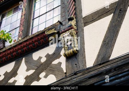 Ein geschnitztes Gesicht schmückt die Fassade eines Gebäudes in Eguisheim, Elsass, und präsentiert kunstvolle Handwerkskunst und Designelemente. Stockfoto