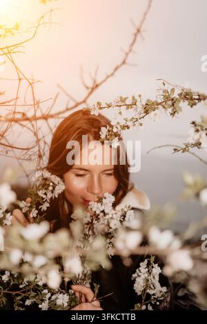 Frau Frühlingsblüte junge Frau, die weiße Kirschblüten in einem blühenden Garten während eines friedlichen Sonnenuntergangs riecht Stockfoto