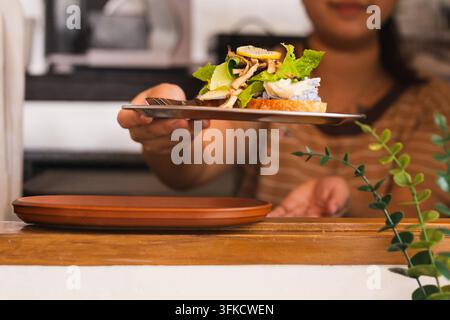 Nahaufnahme einer Frau, die ein frisches offenes Sandwich serviert, das mit grünem Salat garniert ist Stockfoto