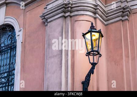 Nahaufnahme einer brennenden antiken schmiedeeisernen Gaslaterne, die die verzierte Wand eines historischen Barockgebäudes beleuchtet. Konzept des romantischen Europas Stockfoto