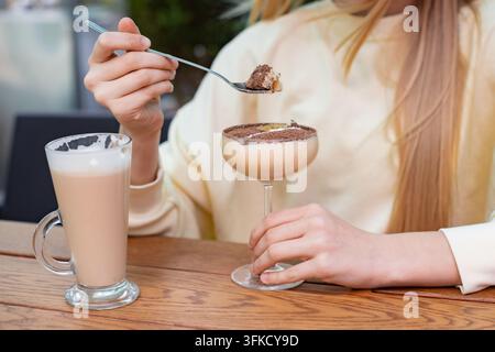 Mädchen isst Schokoladendessert-Mousse und trinkt ein Glas Kaffeelatte im Café, Fokus auf die Hände Stockfoto
