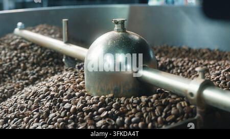 Nahaufnahme von Kaffeebohnen, die durch eine industrielle Mischer- und Trommelröstmaschine in einer Fabrik für die Herstellung von gerösteten braunen Bohnen gedreht werden, automatisierte Ausrüstung Stockfoto