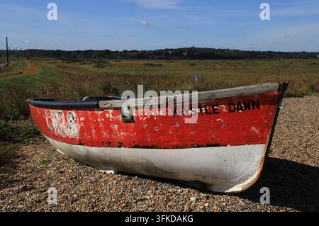 Ein kleines Boot, das auf der landwärts gelegenen Seite des Schotterstrandwalls an der Nord-Norfolk-Küste in Cley next the Sea, Norfolk, England, UK, gestrandet ist. Stockfoto