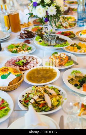 Gäste genießen eine große Auswahl an Gerichten, die auf einem Tisch bei einer Zusammenkunft ausgebreitet sind. Bunte Salate und Fleisch sind vorhanden. Stockfoto