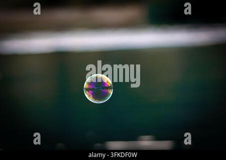 Eine winzige Seifenblase hängt in türkisfarbener Luft mit weichem Bokeh im Hintergrund. Transparente Farben umrahmen die Kugel, während der offene negative Raum Text und Lieferung einlädt Stockfoto