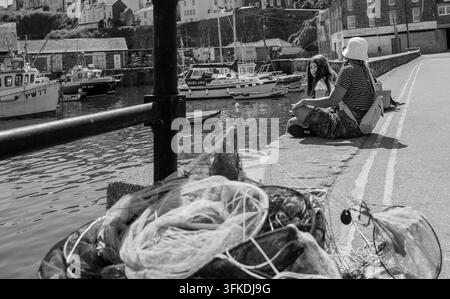 zwei Urlauber, die auf einer Hafenmauer sitzen, einer schaut in die Kamera, Mevagissy, Cornwall Stockfoto