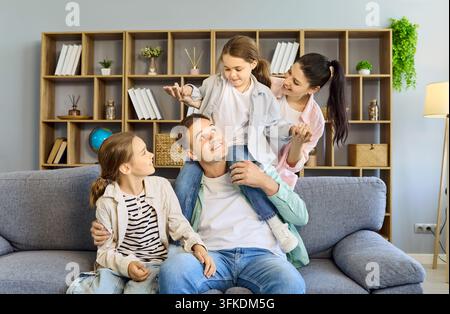 Zufriedene Eltern mit Töchtern, die auf einem gemütlichen Sofa im Zuhause spielen und sich umarmen Stockfoto