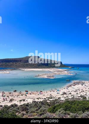 Luftpanorama der Balos-Lagune, Kreta, das türkisblaues Wasser, eine sandige Halbinsel und einen überfüllten Strand unter felsigen Hügeln zeigt Stockfoto