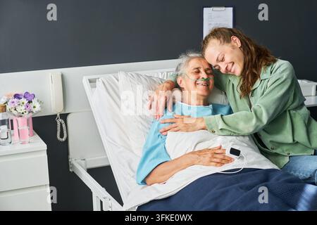 Frau umarmt lächelnde ältere Mutter, die in einem Krankenhausbett ruht Stockfoto