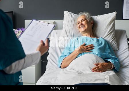 Seniorin ruht sich in einem Krankenhausbett aus und spricht mit einem Arzt Stockfoto