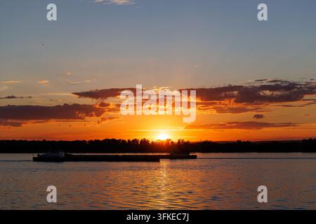 Heller goldener Sonnenuntergang über einem breiten Fluss mit dramatischen Wolken und warmem Abendlicht. Stockfoto