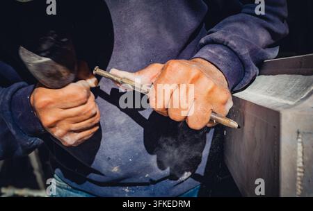 Nahaufnahme eines handwerklichen Steinmetzes, der einen Steinblock mit traditionellen Metallmeißel- und Hammerwerkzeugen in einer Werkstatt schnitzt und formt Stockfoto