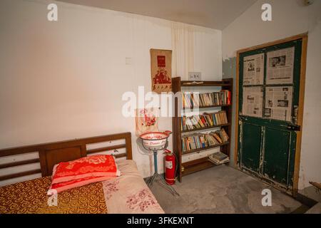 Innenraum eines alten Zimmers mit Holzbetten, Bücherregal und grüner Holztür Stockfoto