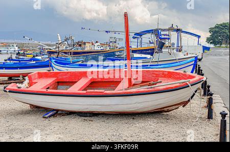 Ein rotes und weißes Holzfischboot ruht am Ufer in der Nähe eines Hafens Stockfoto