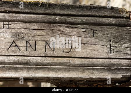 Nahaufnahme einer verwitterten, geschichteten Oberfläche mit dunklen handgeschriebenen oder eingravierten Markierungen, darunter das Wort ANNO. Die gedämpfte braun-graue Textur ist s Stockfoto