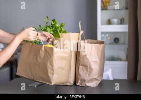 Frische Lebensmittel in braunen Papiereinkaufsbeuteln verpackt, während eine Frau nach der Bestellung zu Hause greift. Konzept von Lebensmittelzustellung, Papierverpackung, onli Stockfoto