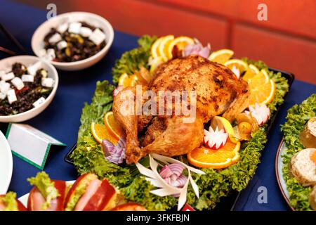 Ein knuspriger ganz gerösteter Vogel, der auf einem Bett aus frischen grünen Salatblättern und Orangenscheiben an einem festlichen Feiertagsbuffet-Tisch platziert ist. Stockfoto