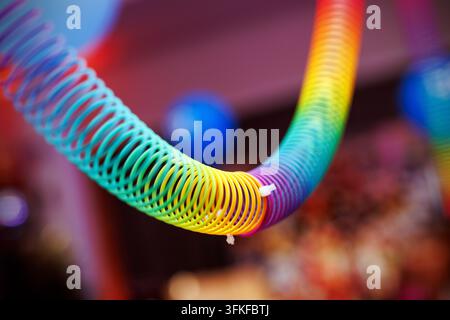 Ein lebhaftes, mehrfarbiges Plastik-Slinky-Federspielzeug schlängelt sich durch das Bild, vor einem weichen, verschwommenen Party-Hintergrund. Stockfoto