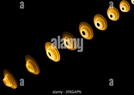 Abstrakter Lichteffekt mit einer Reihe von leuchtenden gelben Kreisen und Ringen, die diagonal auf einem schwarzen Hintergrund angeordnet sind, digitale Grafik. Stockfoto