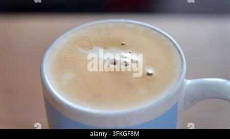 Nahaufnahme einer Tasse Kaffee mit cremigem Schaum und Topping in einer weißen Keramiktasse Stockfoto