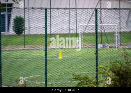 Eine Sicht durch einen grünen Maschendrahtzaun, der auf einen üppigen grünen Fußballplatz mit weißen Grenzlinien, einem Trainingskegel und einem Fußballtor in der Ba blickt Stockfoto