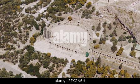 Luftbild, das das historische Odeon des Herodes Attikos zeigt, ein antikes steinernes römisches Theater mit seinen gestuften Sitzreihen und umgebenden grünen Bäumen auf dem A Stockfoto