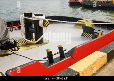 Nahaufnahme von schwarzen Ankerklampen mit dickem weißem Seil und gelb-schwarzer Warnmarkierung auf dem Deck eines Schleppers am Hafenkai Stockfoto