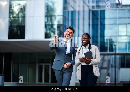Geschäftskollegen gehen und lachen im Freien vor einem Bürogebäude Stockfoto
