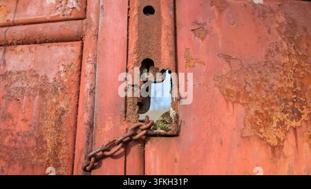 Nahaufnahme eines alten rostigen Metalltors mit einem Schlüsselloch, Riegel und Kette auf einem ländlichen Grundstück im Dorf Sobotiste, Slowakei. Stockfoto