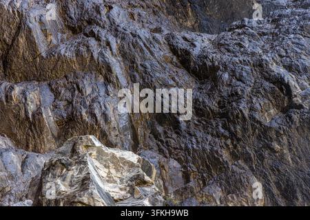 Detaillierte Nahaufnahme zeigt eine nasse Felswand mit einer rauen Textur. Dunkelgraue und schwarze Oberflächen glänzen vor Feuchtigkeit und zeigen geologische Formationen Stockfoto
