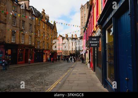 Edinburgh, Schottland, Vereinigtes Königreich – 2. August 2026: Farbfrohe historische Straße mit Fahnen, Geschäften, Touristen und alten Steingebäuden. Stockfoto