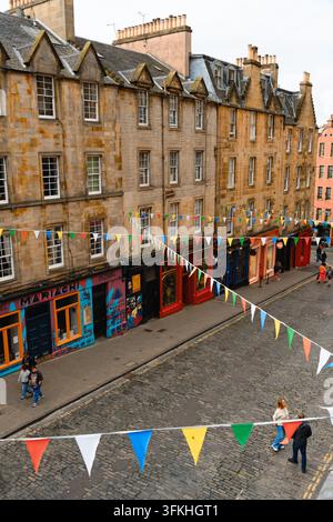 Edinburgh, Schottland, Vereinigtes Königreich - 2. August 2026: Steinerne Tenements, farbenfrohe Fahnen und Ladenfronten säumen die steile Kopfsteinpflasterstraße. Stockfoto