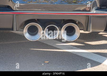 Nahaufnahme eines dunklen Sportwagens, schlanke Karosserie mit Carbonfaser-Details, drei große Auspuffrohre, glänzender Metallkontrast, leicht geneigte Ansicht, Asphalt Stockfoto