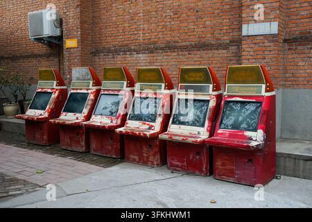 Reihe alter roter Spielautomaten, die vor einer roten Backsteinmauer aufgereiht sind Stockfoto