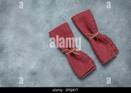 Zwei burgunderrote Leinen servietten mit Schnur gebunden, grauer Grunge-Hintergrund. Oberansicht, Flat Lay. Stockfoto