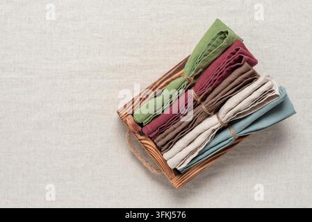 Satz von Leinen servietten gestapelt in einem Holztablett, beiger Leinenstoff als Hintergrund. Oberblick, selektive Schärfe. Stockfoto